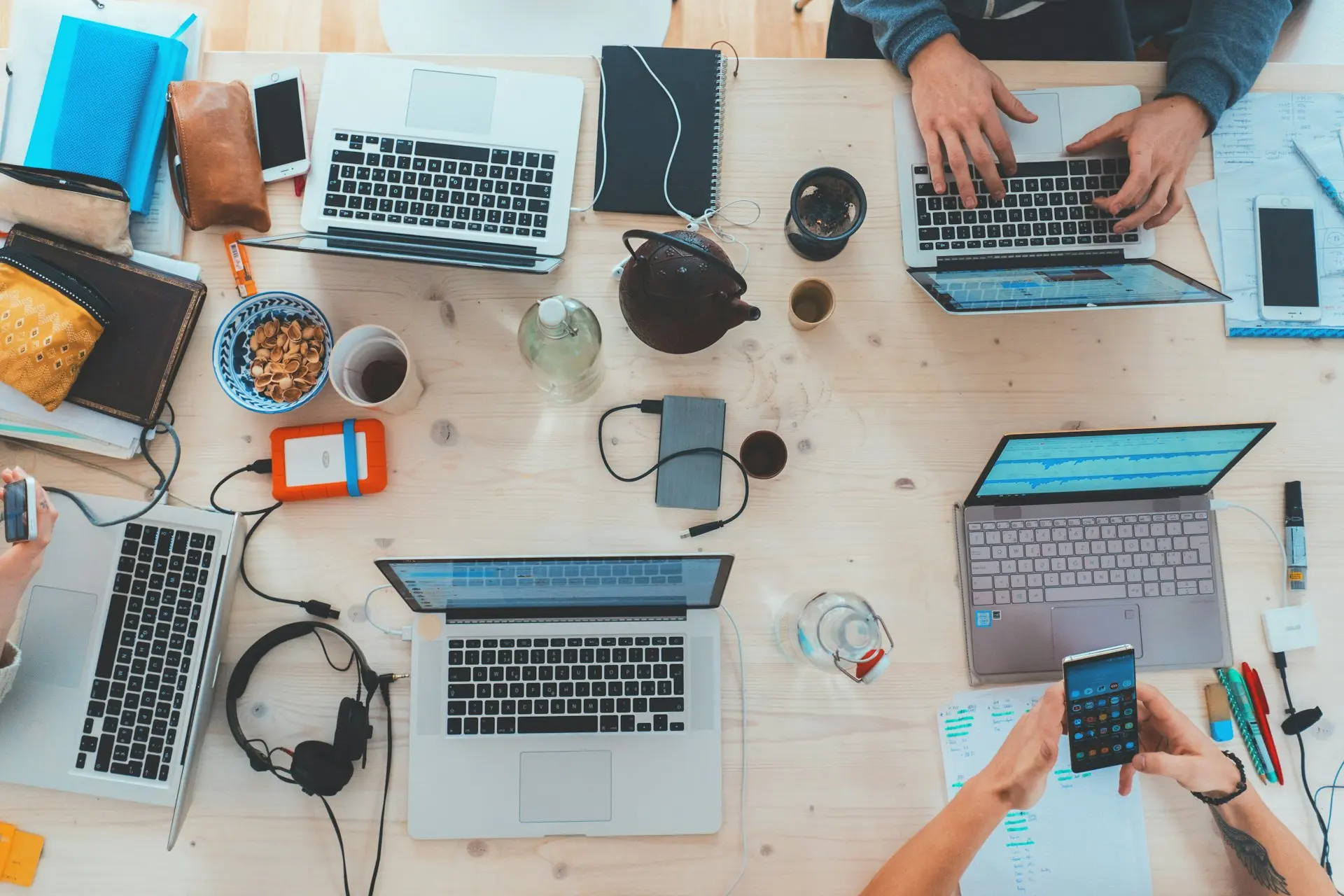 Una scrivania condivisa vista dall'alto, con computer portatili e persone al lavoro